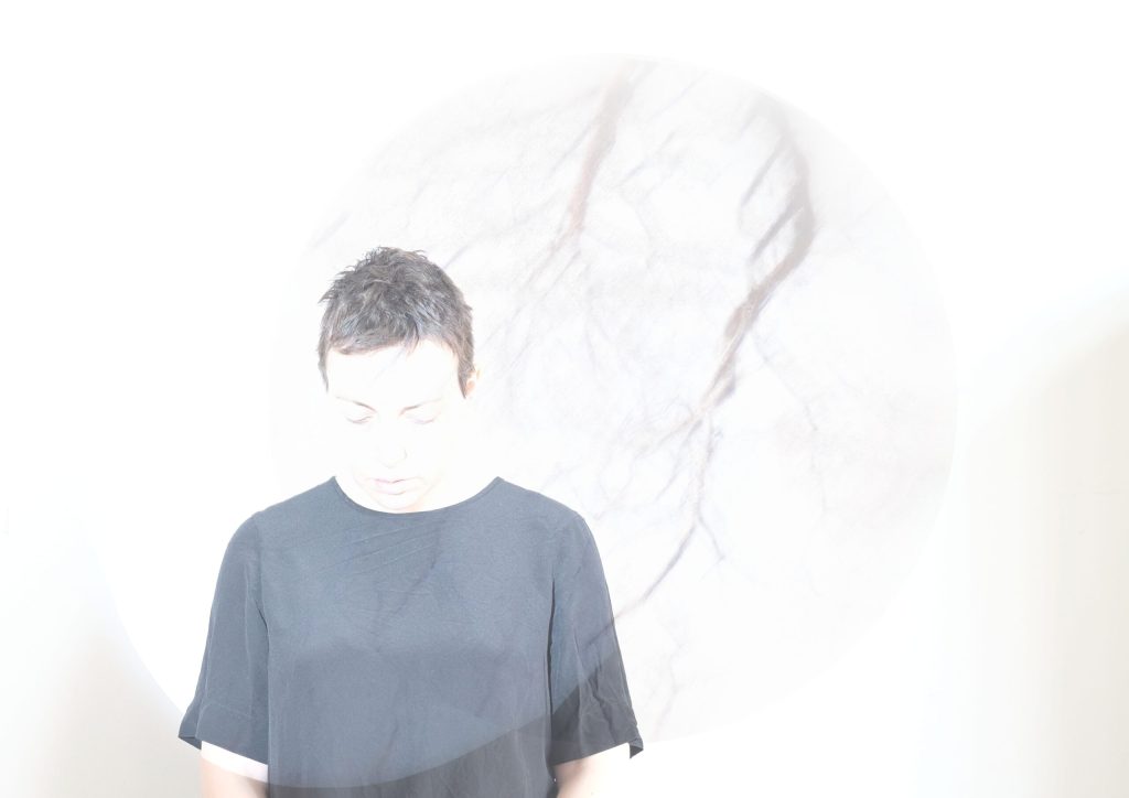 A photo of a person in a black t-shirt, looking down at the floor. The photo is overexposed.