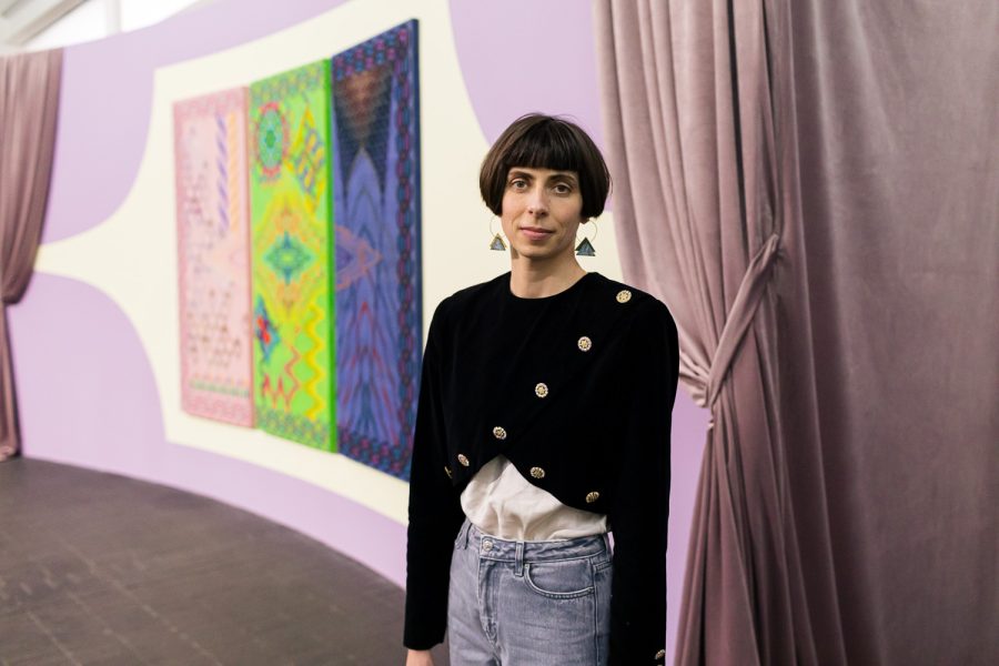 Cecilia leaning against a curtain, behind her is her embroidery installation