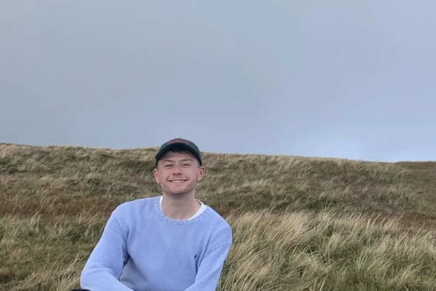 Photo of Dylan crouched in a field smiling at the camera