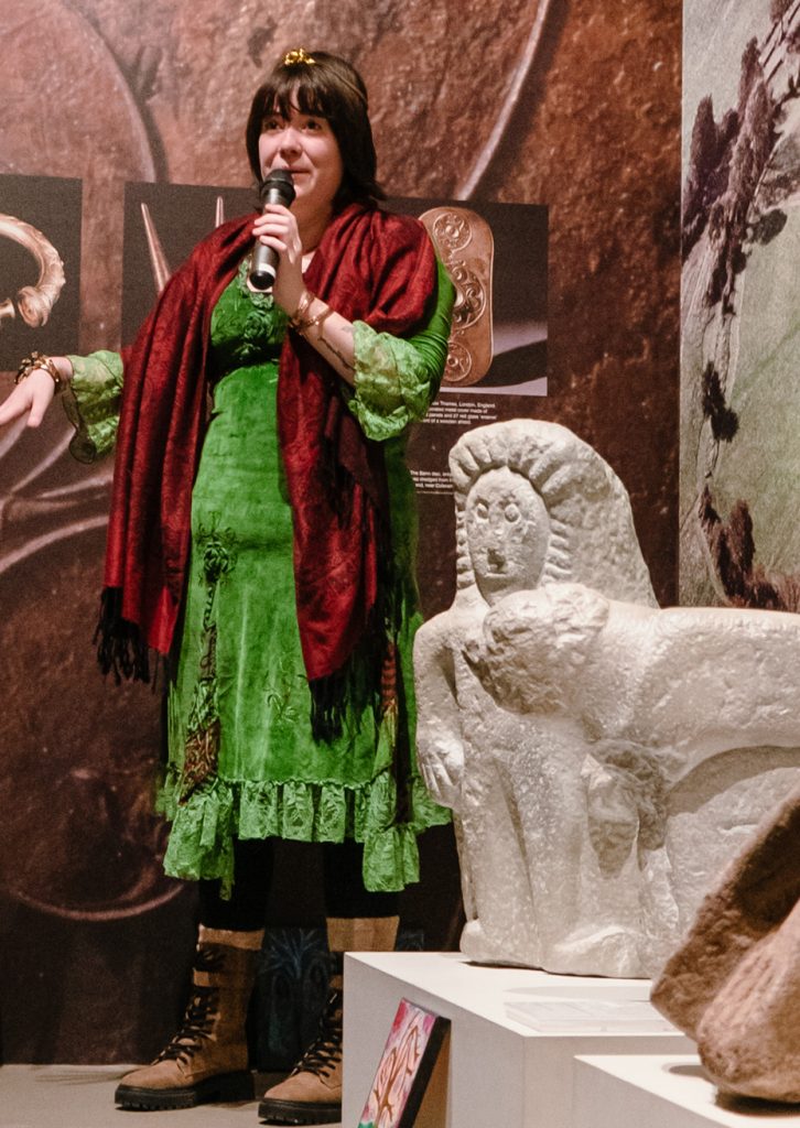 Photo of Maoiliosa standing next to a stone scultpure, holding a microphone